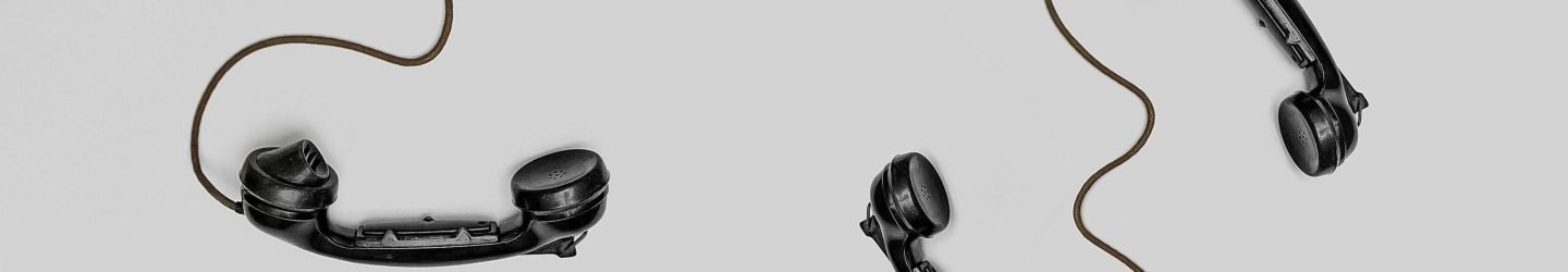 Two vintage black telephone handsets connected by cords on gray background.